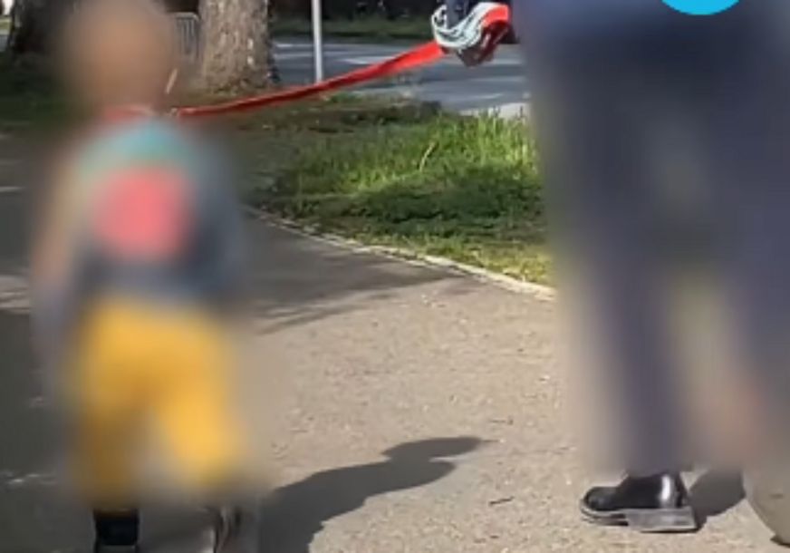 Na Kenedijevom trgu u Zagrebu snimljena je osoba koja vodi malo dijete na povocu. 