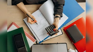 Računovođa analizira finansijske dokumente kalkulatorom na stolu, ističući poslovne zadatke